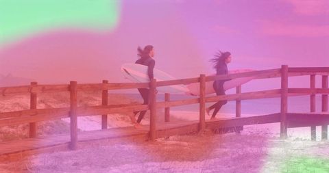 Couple in wetsuits carry surfboards on beach boardwalk