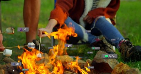 Couple roasting marshmallows over campfire sharing cozy firelight moment with reaction badges