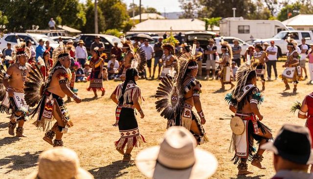 Indigenous dancers wearing feather regalia performing circle dance at outdoor festival