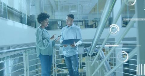 Colleagues discussing tablet and holding laptop on mezzanine with futuristic HUD overlay