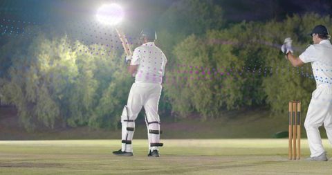 Night cricket match under floodlights batsman holding bat wicketkeeper at stumps
