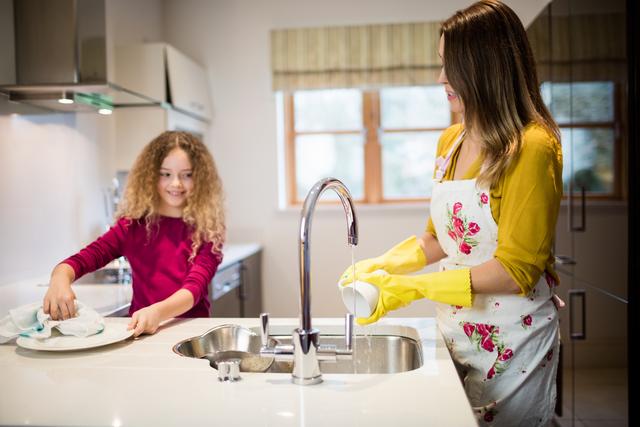 Mother assisting daughter in washing plate in kitchen at home