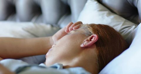 Serene adult woman resting on bed with tufted headboard and soft pillows, closeup portrait