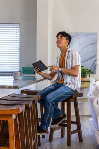 Young asian man working remotely on tablet at kitchen breakfast bar