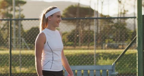 Smiling Female Tennis Player Holding Ball on Grass Court at Sunset