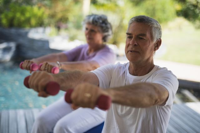 Senior man exercising with woman while holding dumbbells