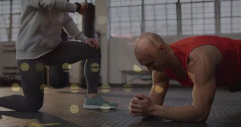 Trainer monitoring forearm plank exercise in gym
