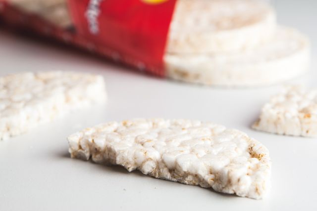 This image shows a half-eaten rice cake placed on a white table with other rice cakes in the background. Suitable for articles on healthy snacking, diet plans, and nutritious food options. It can also be used in marketing materials for health-focused food brands or lifestyle blogs.