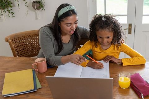 Home tutoring moment: caregiver guiding schoolgirl through homework with laptop notebook