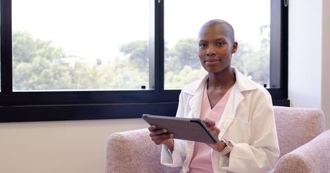 African female clinician using digital tablet while sitting by window in modern medical office