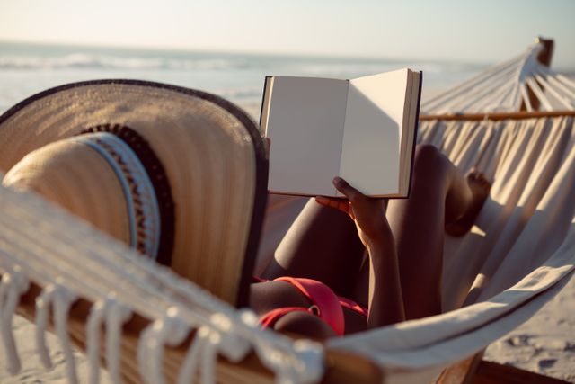 Young woman reading a book while relaxing in hammock on the beach