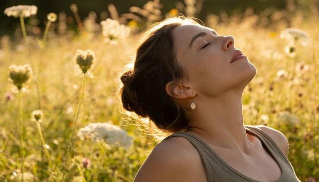 Young woman breathing in sunlit meadow, relaxing during golden hour with bokeh