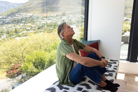 Middle-aged man sitting on sunny window seat, relaxed and contemplative home moment