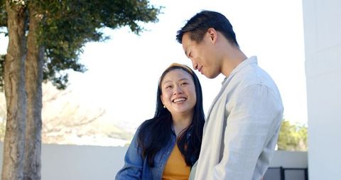 Asian couple laughing and talking on sunlit terrace enjoying casual outdoor lifestyle