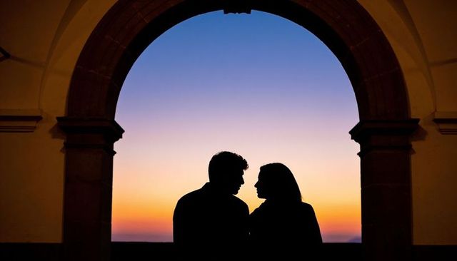 Silhouetted couple framing sunset through historic stone archway over calm seascape