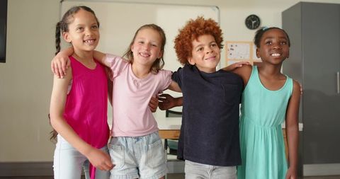 Smiling diverse children linking arms in classroom showing friendship and teamwork
