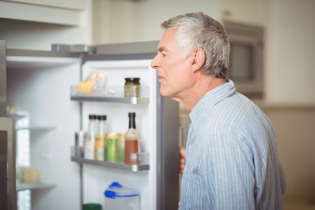 Senior man looking inside refrigerator in kitchen at home. Perfect for illustrating domestic life, elderly lifestyle, and everyday activities. Useful for articles or advertisements related to home appliances, senior living, and nutrition.