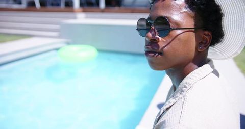 Relaxing poolside wearing wide-brim hat and round sunglasses, neon float in turquoise water