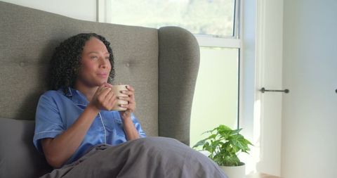 African american woman sipping coffee in bed, relaxing in satin pajamas, morning calm
