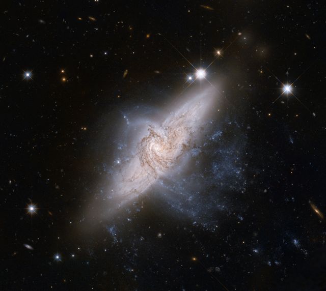 Two galaxies are visibly colliding against a backdrop of numerous bright stars in deep space. The interaction between these massive celestial structures creates a striking, almost symmetrical pattern, hinting at the powerful forces at play. This visual is perfect for educational materials on astronomy, space-themed backgrounds, or articles discussing cosmic events and phenomena.