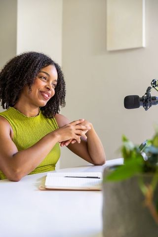 African american woman hosting podcast in minimalist studio with microphone and notebook