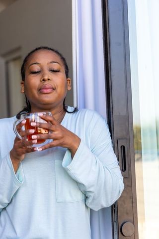 Morning calm: african american woman enjoying tea at balcony sliding door