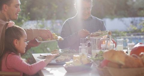 Multigenerational family sharing sunlit outdoor dinner around garden table during summer