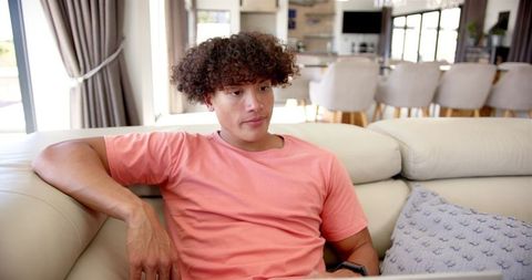 Relaxed Young Man with Curly Hair sitting on Cosy Sofa