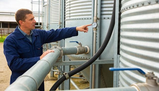 Farmer checking pressure gauge on grain silo during routine equipment inspection
