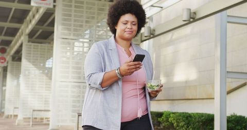 Confident Professional Carrying Salad and Phone Walking in Urban Landscape