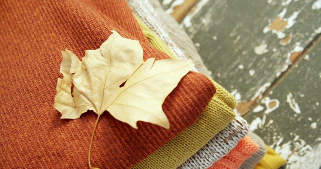 Close up of stack of blankets and autumn leaf on wooden background. Autumn, fall, nature and seasons concept.