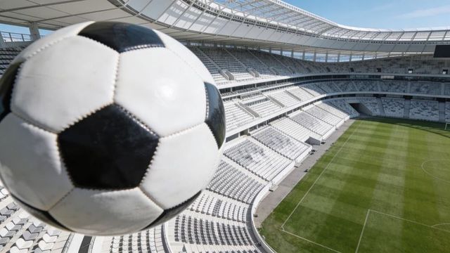 Close-up classic soccer ball dominating left frame with empty modern stadium and pitch
