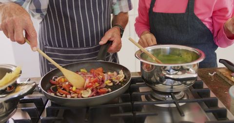 Senior couple cooking together in kitchen wearing aprons