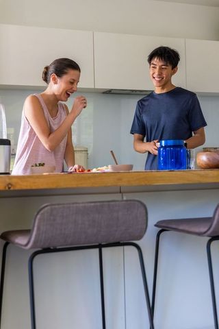 Laughing diverse couple preparing healthy meal at modern kitchen island with barstools