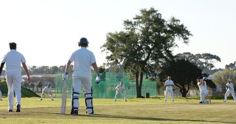 Cricket match in action with players on green pitch under sunny sky