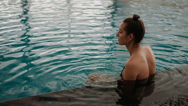 Serene woman relaxing at pool edge gazing outward, contemplative swimwear lifestyle scene