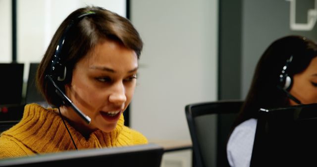 Close up of young customer service executives talking on headset at desk in office. The casual dressed woman is talking to a client.