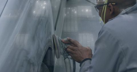 Technician sanding primed car fender wearing respirator and coveralls in autobody bay