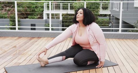 African American Woman Doing Seated Forward Stretch on Rooftop Yoga Mat in Pink Activewear