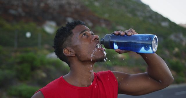 African american man drinking water while standing on the road. fitness sports and healthy lifestyle concept