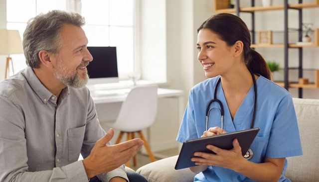 Home telehealth nurse consulting with mature male patient on tablet, friendly discussion