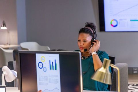 African american woman analyzing data dashboards on dual monitors in modern office