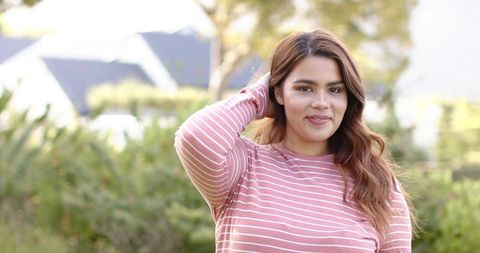 Young woman posing in suburban yard wearing striped long-sleeve top in sunlight