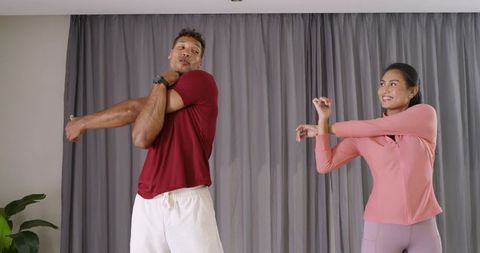 Asian Woman and African American Man Doing Shoulder Stretches at Home Workout in Activewear