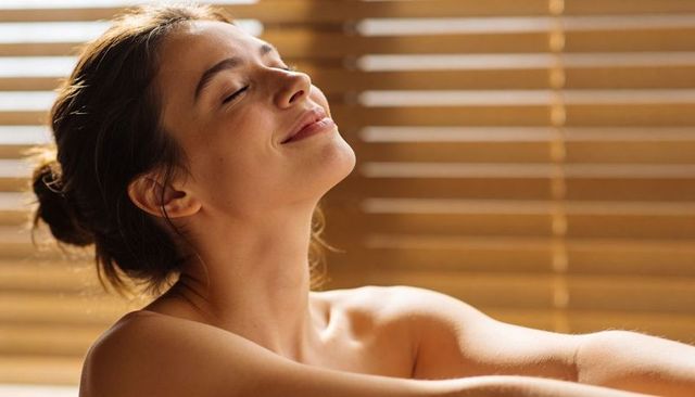 Sunlit spa moment woman relaxing with closed eyes and wooden blind light stripes