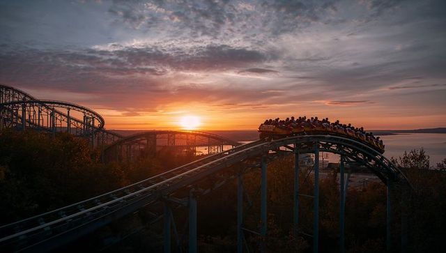 Roller coaster enters sunset drop, filling sky with adventure and thrill