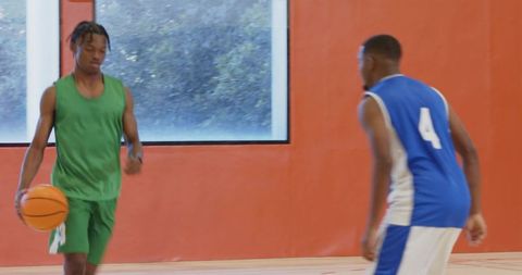 Basketball guard dribbling past defender on indoor gym court with orange wall