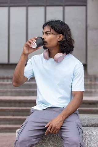 Adult african american man drinking coffee with pink headphones on urban steps