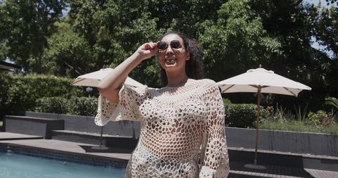 African american woman adjusting sunglasses at pool in white crochet cover-up