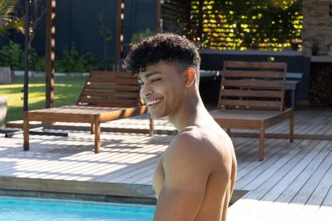 African american man smiling over shoulder by pool on sunny wooden deck